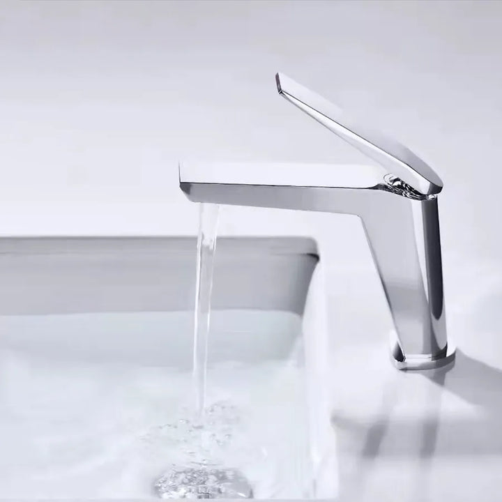 Un robinet lavabo minimaliste en laiton argenté chromé avec de l'eau qui coule. Parfait pour une salle de bain au design épuré et élégant.
