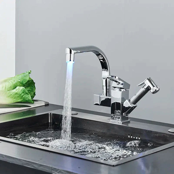 Un robinet d'évier de cuisine en laiton argenté brossé ou chromé avec LED illuminant l'eau qui s'en écoule. Bec pivotant à 360° et douchette pistolet flexible.