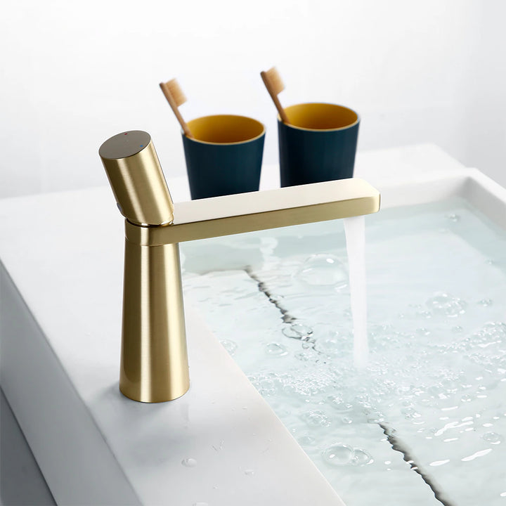 Un robinet lavabo minimaliste en laiton doré brossé avec de l'eau qui s'écoule. Ajoutez une touche d'élégance moderne à votre salle de bain avec ce robinet géométrique design.