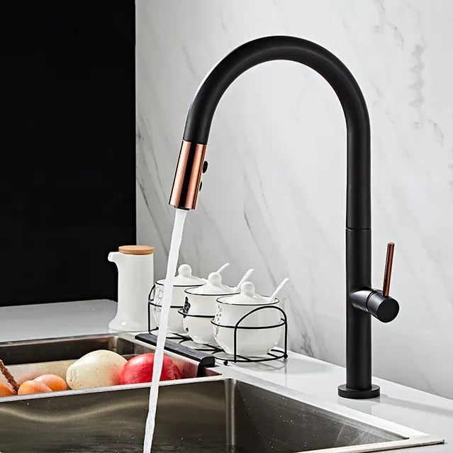 Un robinet évier cuisine avec de l'eau qui coule, une douchette dorée rose et un bec noir cylindrique. Design minimaliste et élégance contemporaine. Matériau en laiton. Dimensions : 437 x 218 mm. Parfait pour votre cuisine.