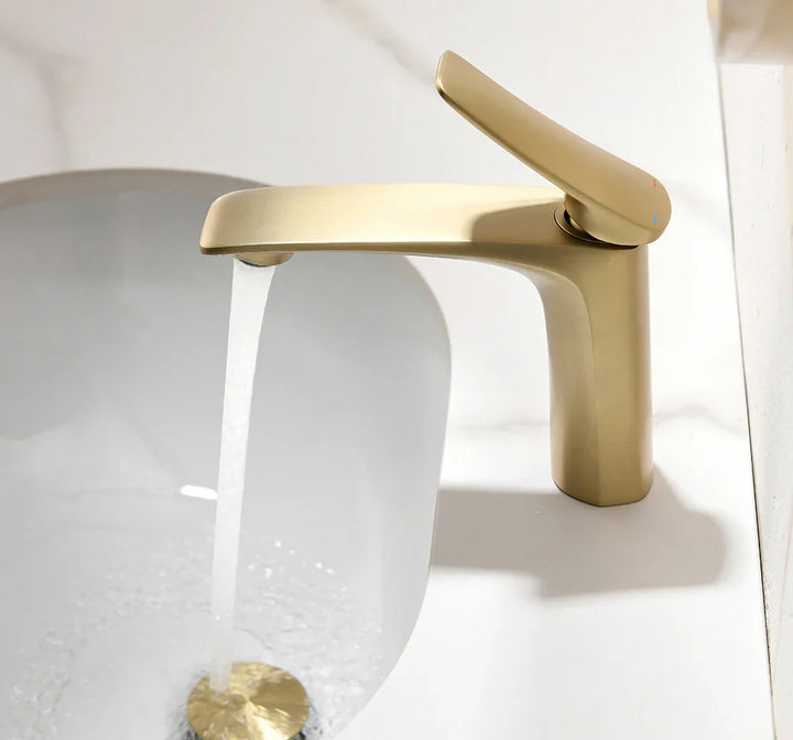 Dans une salle de bain en marbre, un robinet doré brossé minimaliste est installé. 