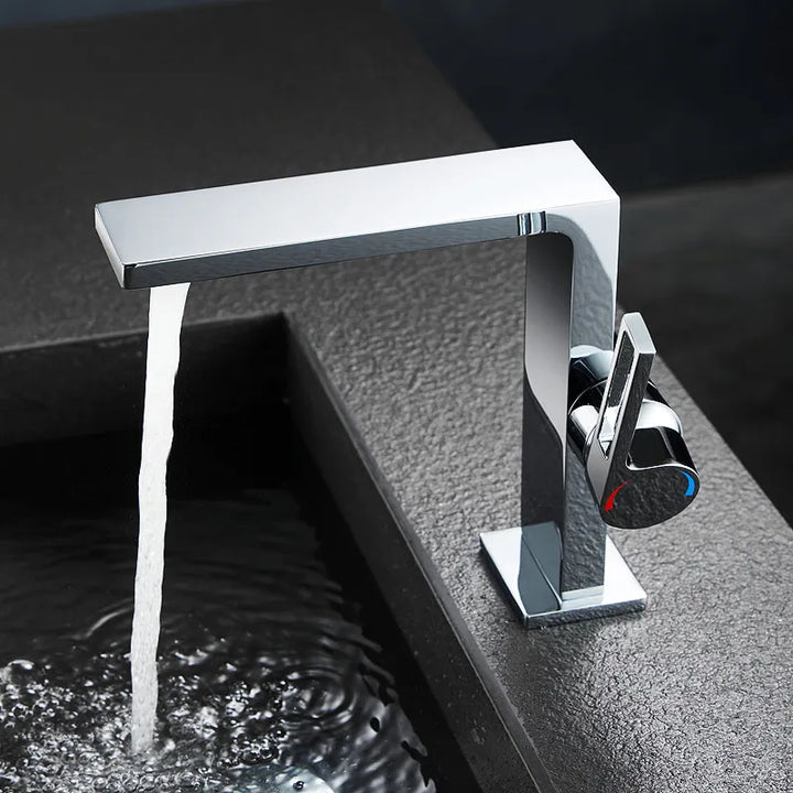 Un robinet de salle de bain plat rectangulaire minimaliste en laiton argenté, avec de l'eau qui s'écoule. Poignée de mitigeur ronde et allongée.