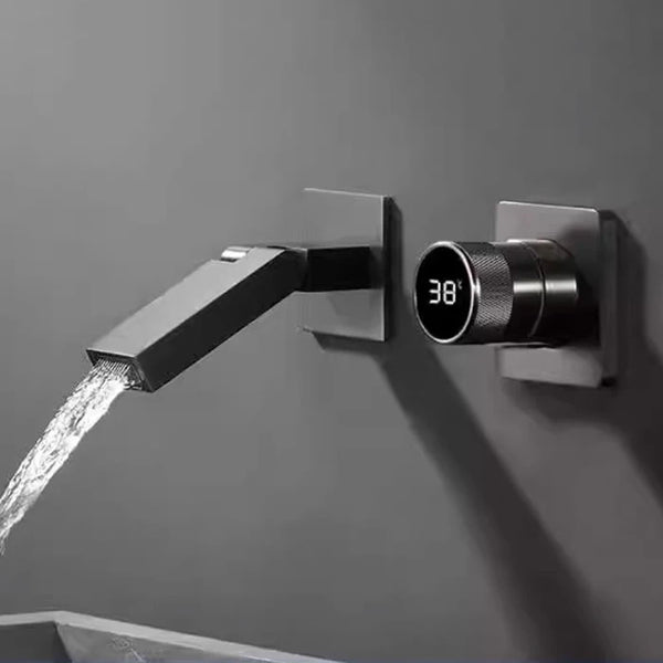 Un robinet pour lavabo de salle de bain est argenté anthracite et encastré au mur. Il est mural, minimaliste avec un bec pivotant à 360° et à côté une poignée avec affichage de la température numérique.