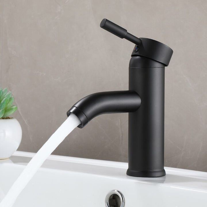 Un robinet lavabo salle de bain minimaliste mitigeur en noir mat avec de l'eau qui en sort. Design élégant en acier inoxydable pour une durabilité et une résistance optimales. Poignée ergonomique pour une manipulation confortable. Disponible en deux hauteurs pour s'adapter à votre vasque.