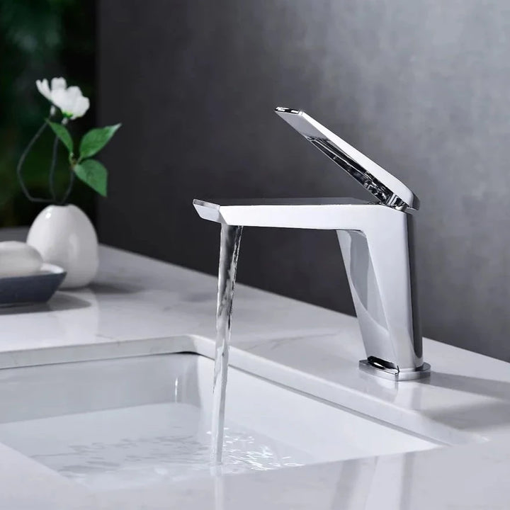 Un robinet lavabo minimaliste en laiton argenté chromé, avec un mitigeur rectangulaire sur le dessus. Parfait pour une salle de bain au design épuré et une finition impeccable.