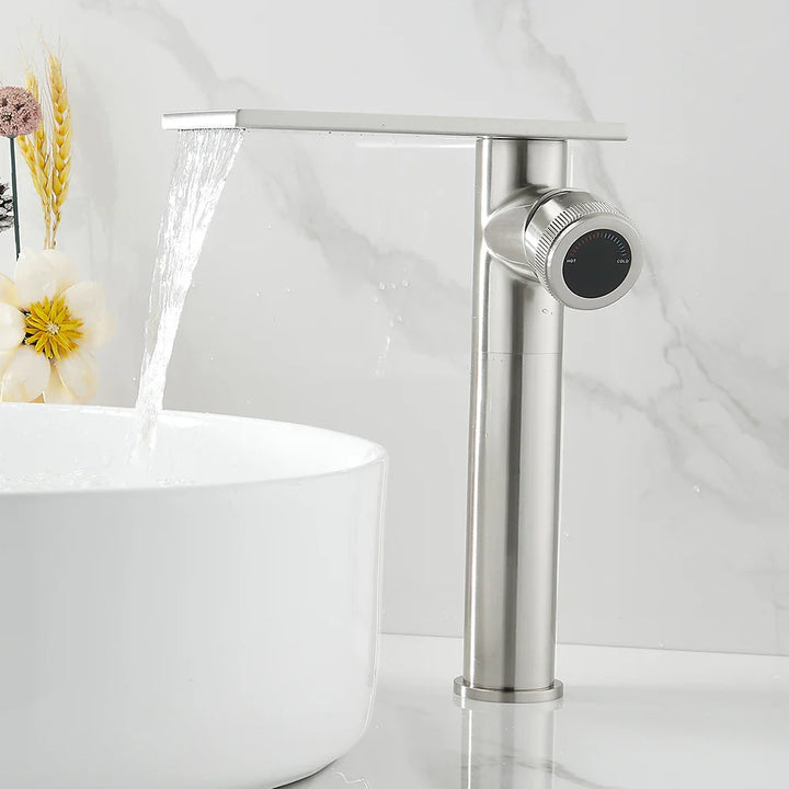 Dans une salle de bain, un lavabo est installé avec un robinet à bec plat et poignée sur le côté. Le robinet est argenté. 