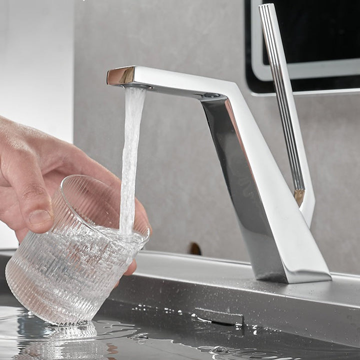 Un robinet salle de bain lavabo mitigeur design contemporain - Argenté, en acier inoxydable, avec une personne versant de l'eau dans un verre.