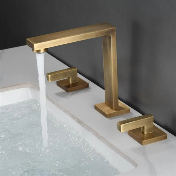 Dans une salle de bain, un robinet minimaliste doré bronze brossé avec deux poignées déportées est installé sur un lavabo.