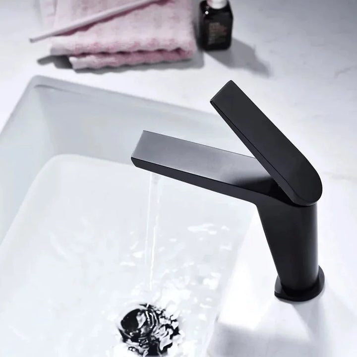 Un robinet lavabo minimaliste en laiton noir mat avec eau qui coule. Forme épurée avec mitigeur rectangulaire sur le dessus. Filtre aérateur nid d'abeille pour une sortie d'eau fluide et agréable. Dimensions : 166 x 140 mm. Poids : 1,135 kg. Idéal pour une salle de bain au design minimaliste.