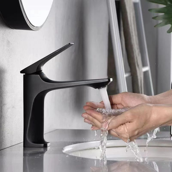 Dans une salle de bain, une main ouvre un robinet de lavabo. Le robinet est noir brossé dans un design épuré.